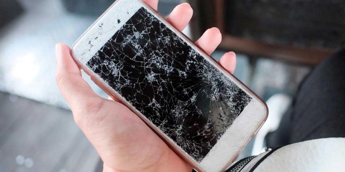 A hand holding a smartphone with a cracked screen, displaying multiple spiderweb-like fractures