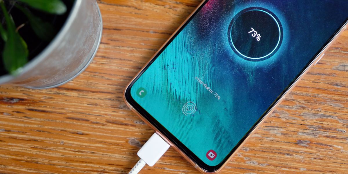 A smartphone charging with a 73% battery level displayed on its screen, alongside a small plant.