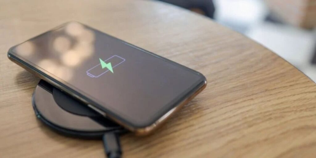 A smartphone placed on a wireless charger, showing a battery icon with a green charging symbol on the screen.