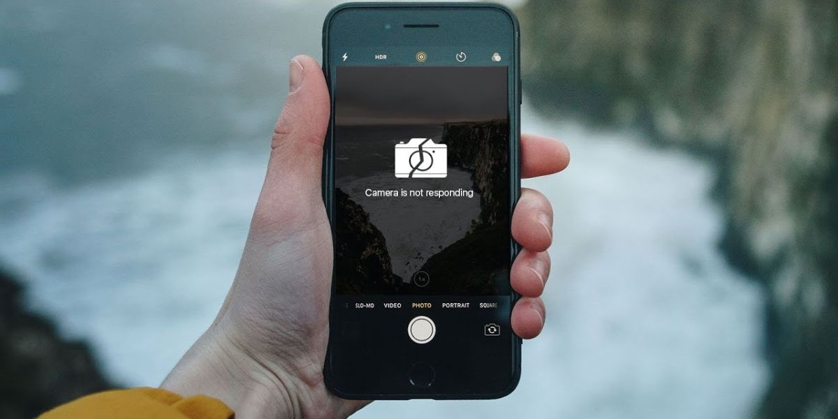 Hand holding a smartphone showing a "Camera is not responding" error over a cliff background.