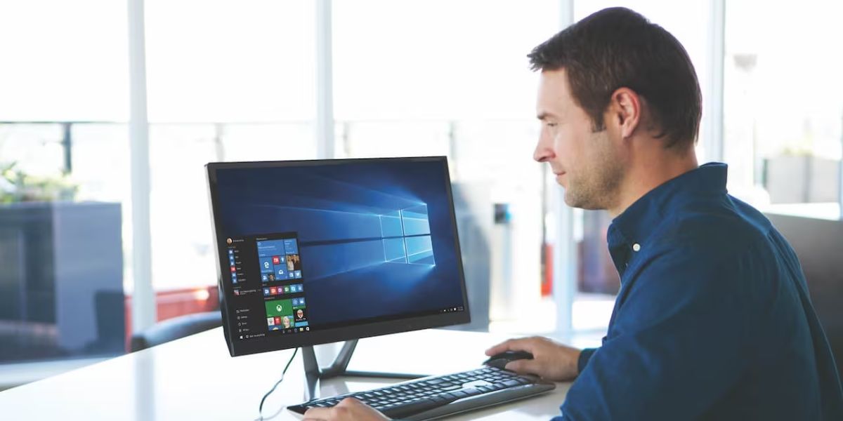 Man working on an All-in-One PC displaying the Windows 10 desktop in a bright office