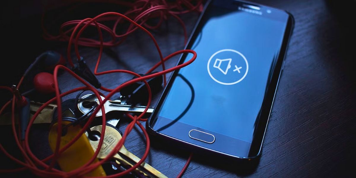 Smartphone displaying a "Mute" icon next to keys and tangled red headphones on a dark table