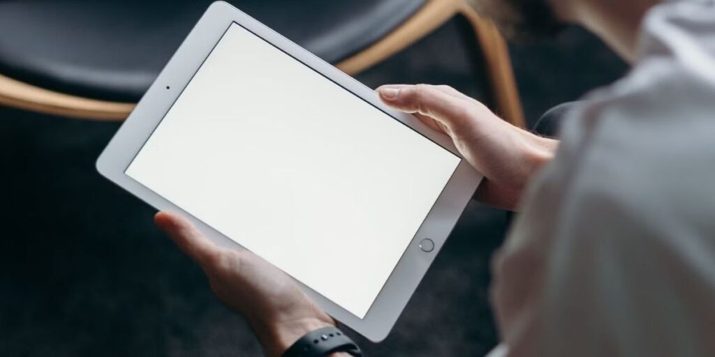 Man holds a white tablet with a blank, white screen in a dimly lit indoor setting