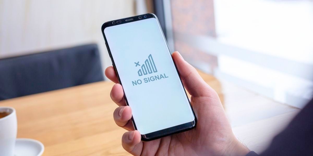 A hand holds a smartphone displaying a "NO SIGNAL" message with a crossed-out signal icon on a white screen