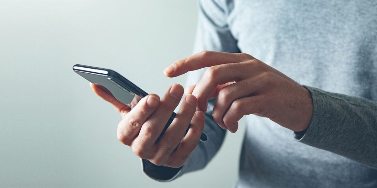 Man's hands in a gray shirt operating a black smartphone with his index finger
