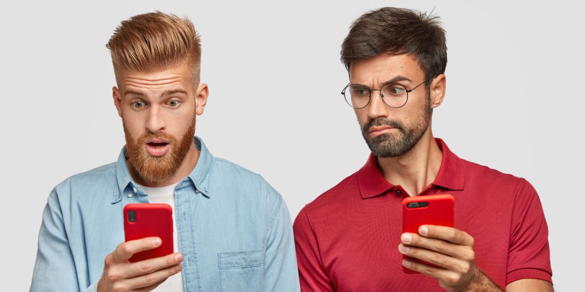 Two men look at their red iPhones with surprised and confused expressions against a plain light gray background